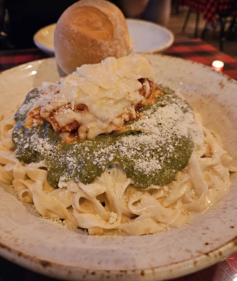 Fresh fettuccine plated half with house pesto and half with creamy parmesan, a sourdough bun on the side