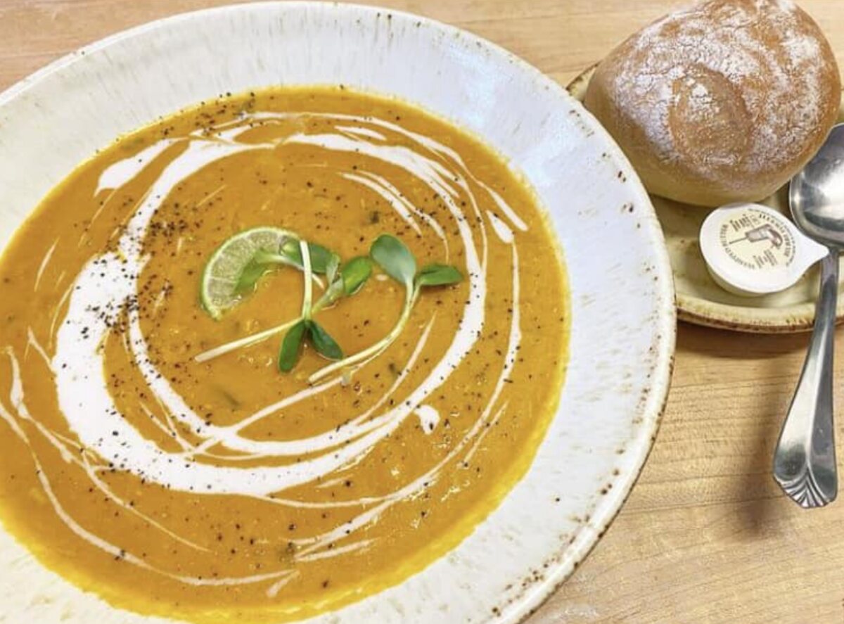 A wide bowl of roasted squash soup swirled with cream, with a sourdough roll and butter