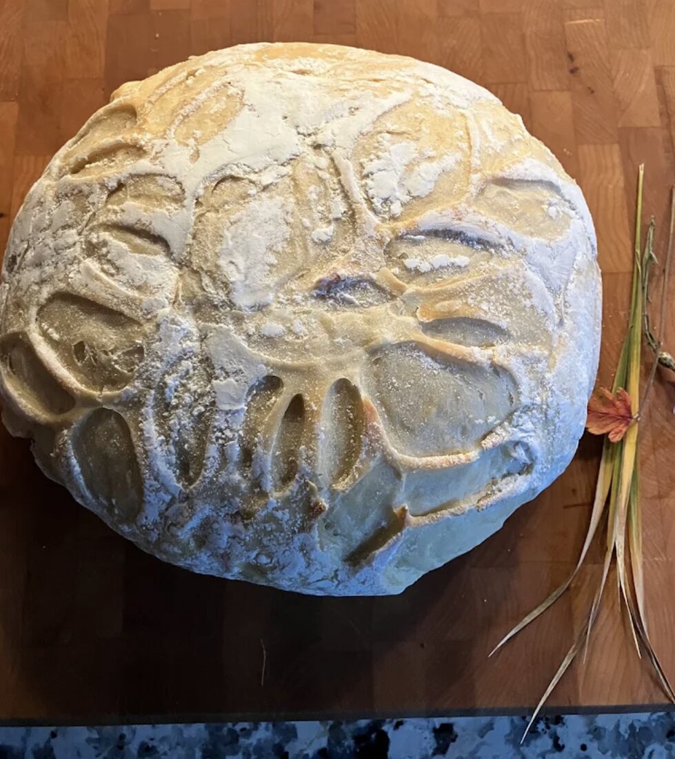 A round sourdough loaf scored with a Bigfoot footprint, fresh from the oven