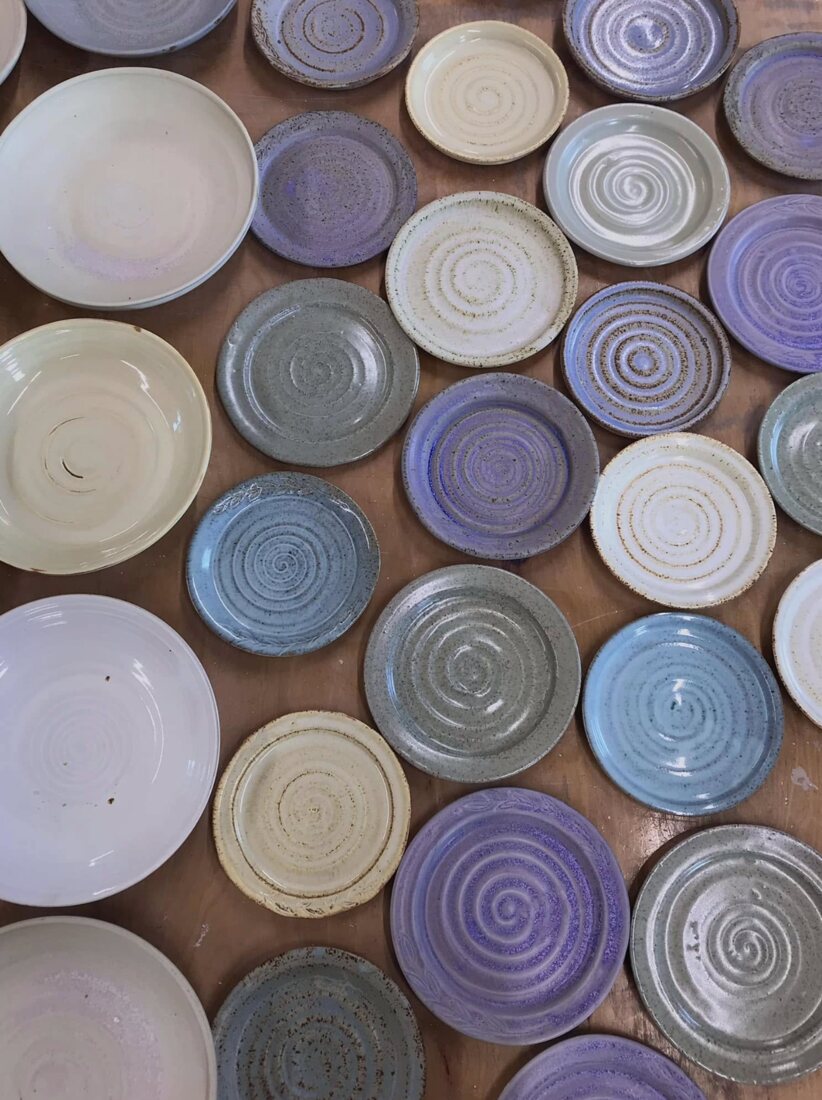 Rows of hand-thrown shallow bowls glazed in blues, purples and cream