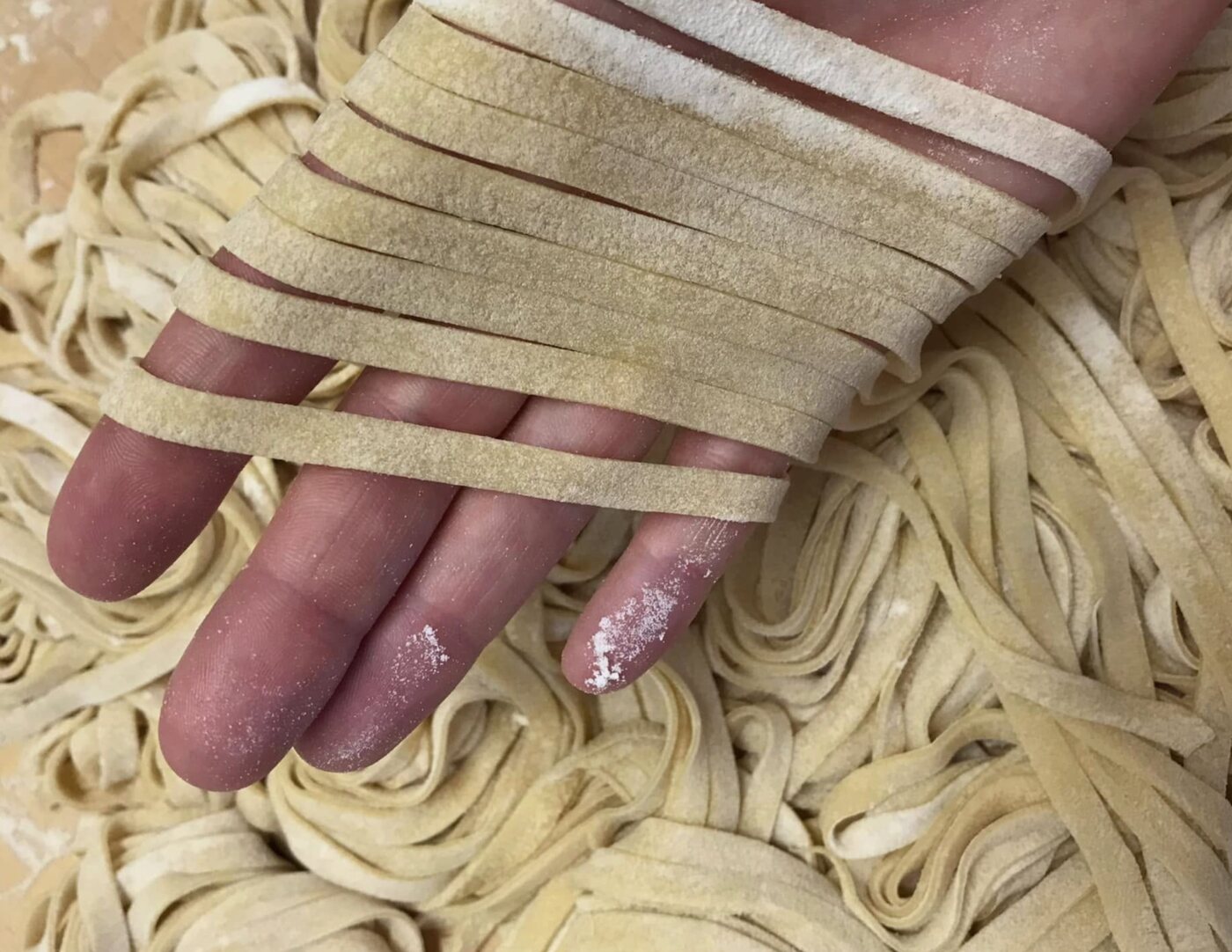 A hand draped with fresh-cut fettuccine ribbons over a tray of just-rolled pasta
